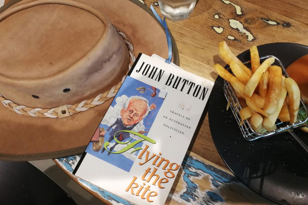 Book Flying The Kite sitting on a table next to a leather hat and a plate with chips and a burger